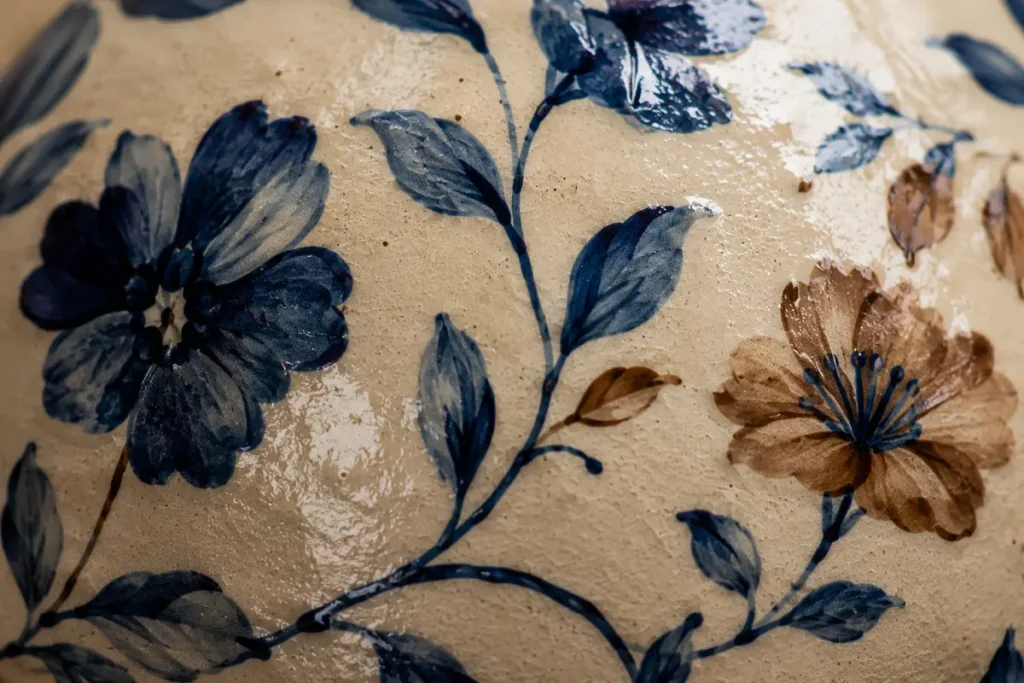 Close-up of hand-painted blue and brown floral motifs on a cream-glazed Khurja ceramic